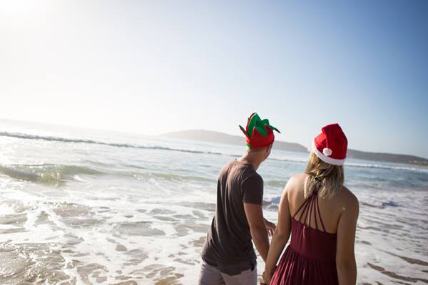 Niño y niña en la playa con sombreros de navidad